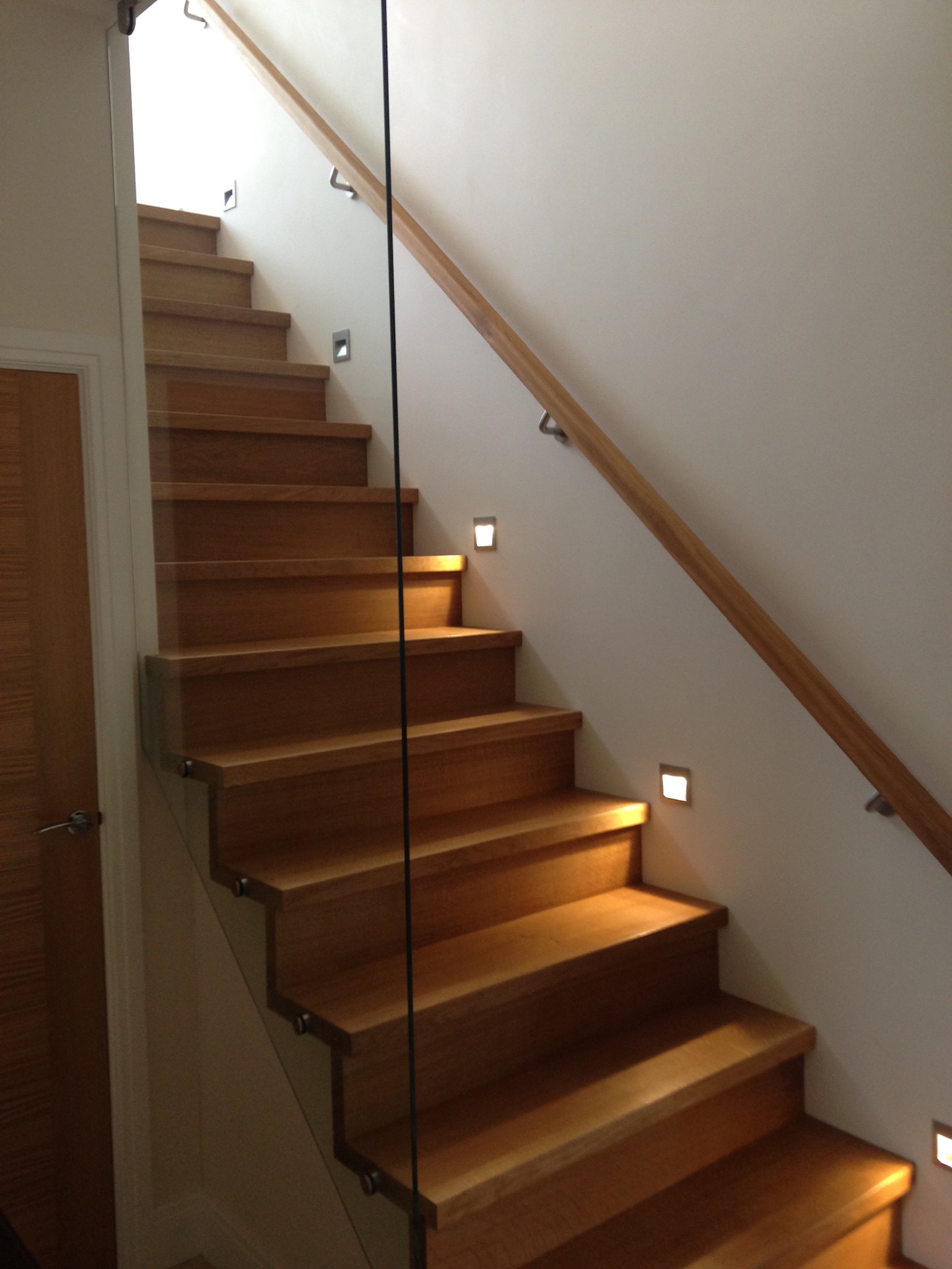 Timber stair treads and handrail beside a glass balustrade and recessed step lights