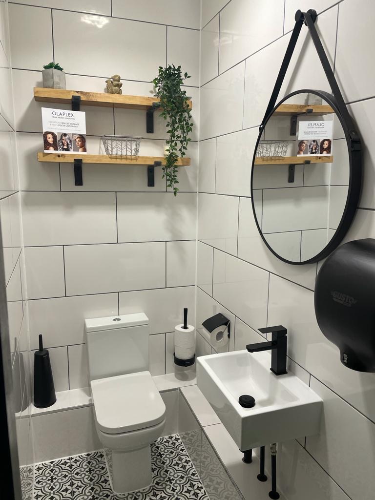 White tiled cloakroom with patterned flooring, timber shelves, a round black mirror and a compact wall-mounted basin