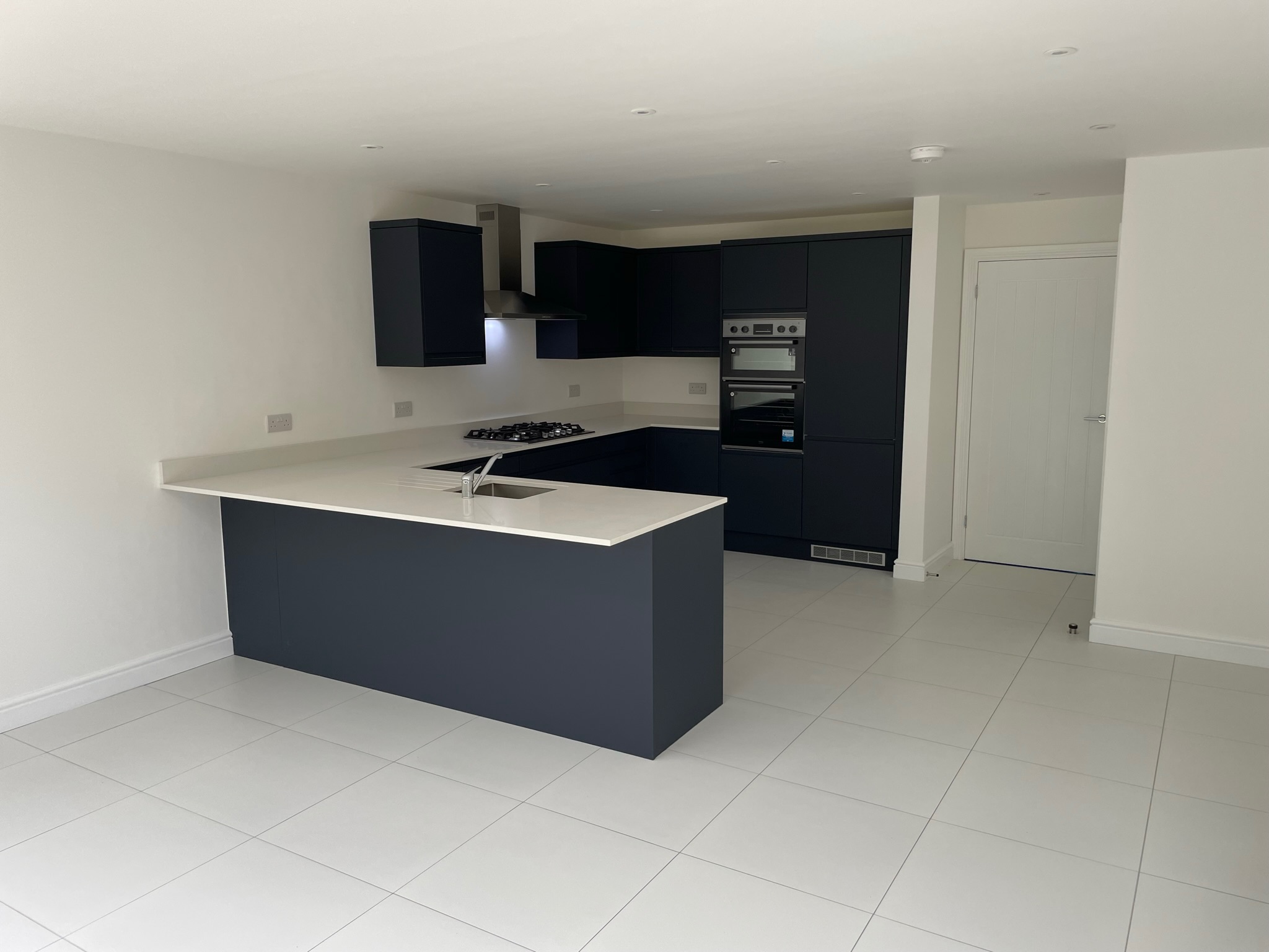 Dark kitchen cabinetry with pale worktops and a peninsula