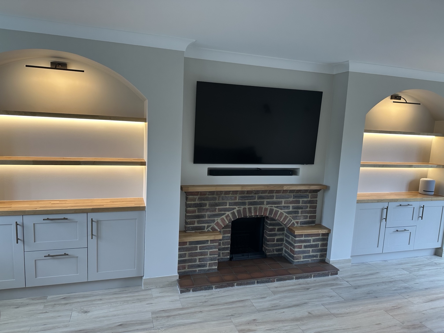 Illuminated alcove shelving and fitted cupboards beside a brick fireplace