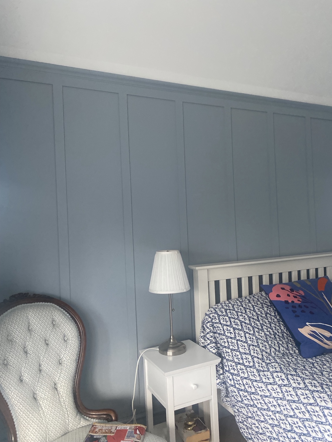 Blue painted vertical rectangular wall panelling behind a white bed and bedside lamp